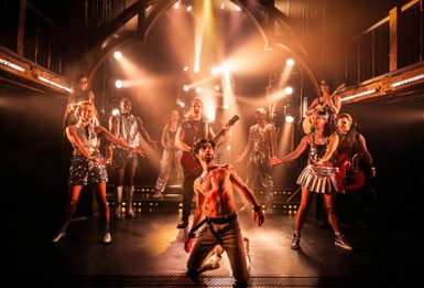 The cast of Jesus Christ Superstar on stage. Jesus is kneeling at the front of the stage with Judas stood behind him playing an electric guitar.