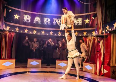 A Barnum production photo with an acrobat holding another acrobat above their head