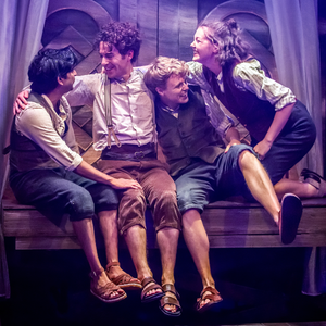 Four Hobbits sitting on a wooden bench hugging and smiling at each other.