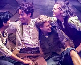 Four Hobbits sitting on a wooden bench hugging and smiling at each other.