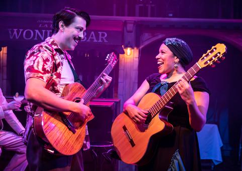 A man and a woman hold guitars and are facing each other smiling