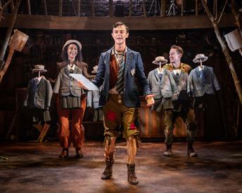 A Pinocchio production shot, with Pinocchio in a school jacket and tie holding a book and two actors with small uniforms in front of their costumes as well as holding extra uniforms to give the impression of lots of children
