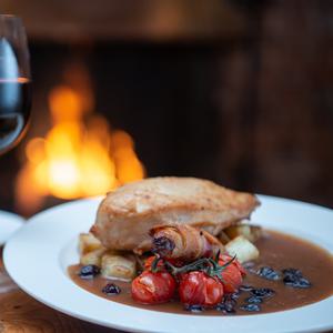A roast chicken dinner served with a glass of red wine in front of a roaring log fire