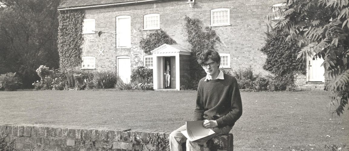 David Gollins sits on a bridge with the Watermill Theatre in the background.