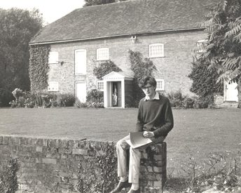 David Gollins sits on a bridge with the Watermill Theatre in the background.