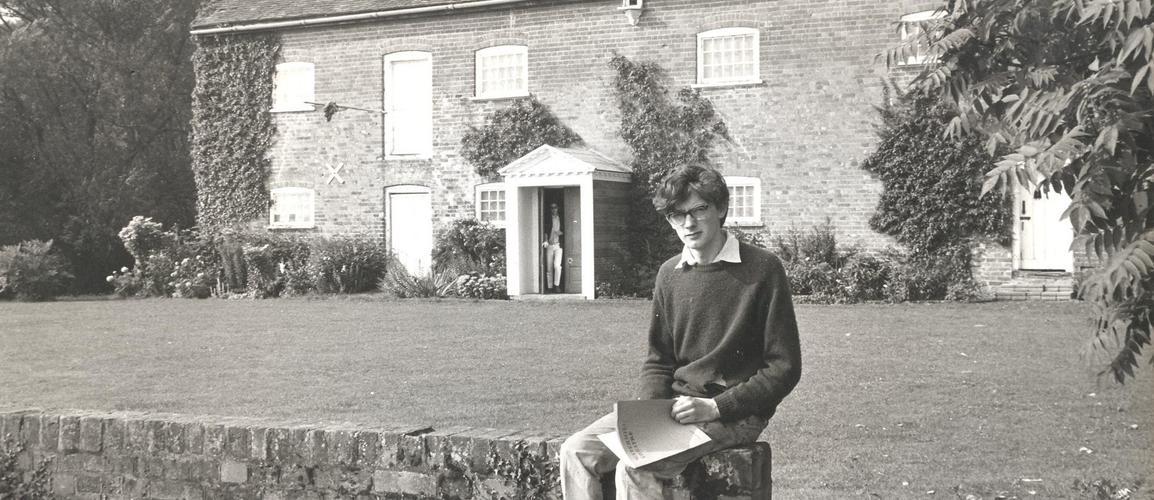 David Gollins sits on a bridge with the Watermill Theatre in the background.