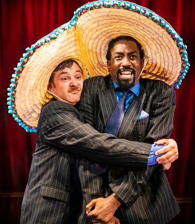 Two men in suits and sombreros hug each other
