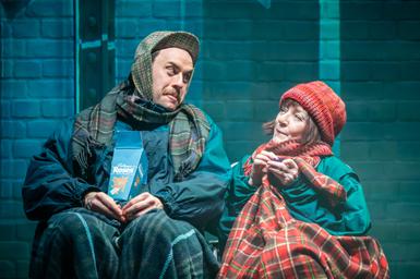 Two people wrapped up warm sit on a bench sharing a box of Roses chocolates