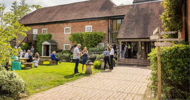 A path leading up to the Watermill Theatre with customers sat on benches on the front lawn.