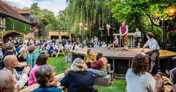 An audience sat on benches around a circular stage on the Watermill back lawn.